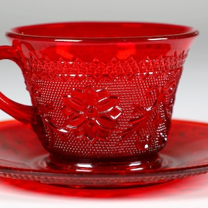 May include: A vibrant ruby red glass teacup and saucer. The cup has a floral pattern and textured details. The saucer has a beaded edge. This vintage tea set is ideal for serving tea or coffee.