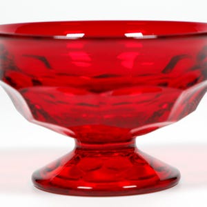 May include: A red glass pedestal bowl with a faceted design. The bowl is made of ruby red glass and has a classic, elegant shape.