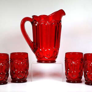 May include: A set of seven red glass pieces, including a jug and six tumblers. The glasses and jug have a textured, raised pattern of circles and stars.