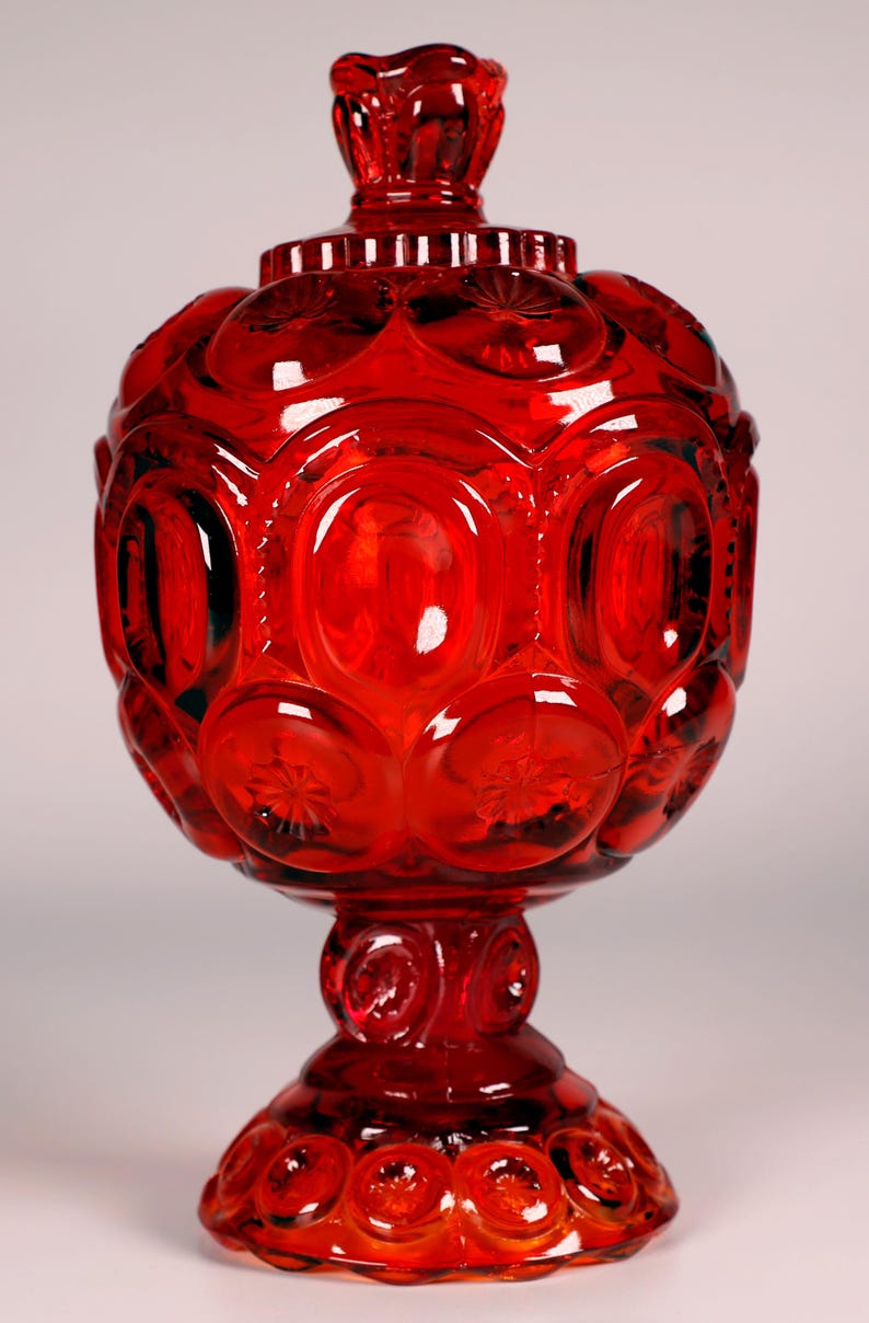 Puede incluir: Un plat de dulces de vidrio rojo con una base de pedestal. El plato est&aacute; decorado con un patr&oacute;n repetitivo de peque&ntilde;os c&iacute;rculos y estrellas.