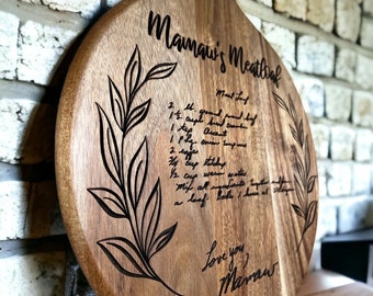 May include: A round wooden cutting board with a handle, engraved with a handwritten recipe for Mamaw's Meatloaf, along with a floral design and the words "Love you, Mamaw".