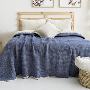 May include: A blue bedspread with a textured weave covers a bed, complemented by white pillows and a decorative basket. The bed is set against a light wooden headboard and a matching side table.