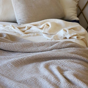 May include: A bed with neutral-toned bedding. The bed has two pillows and a folded blanket in shades of beige and cream. The headboard is made of bamboo.