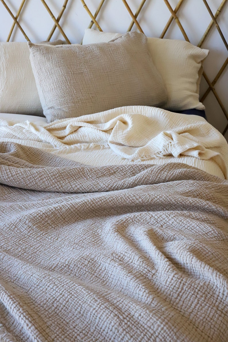 May include: A bed with neutral-toned bedding. The bed has two pillows and a folded blanket in shades of beige and cream. The headboard is made of bamboo.