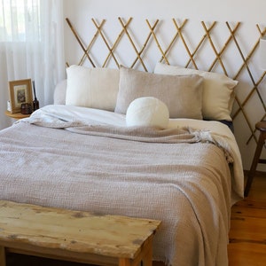 May include: A bedroom with a bed featuring a bamboo headboard and neutral-toned bedding. The bed has a textured, light brown blanket and several pillows. A wooden bench is at the foot of the bed, and the room has hardwood floors.