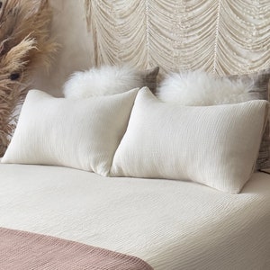 May include: A white bed with a white quilt and two white pillows. The bed has a pink throw blanket at the foot of the bed.