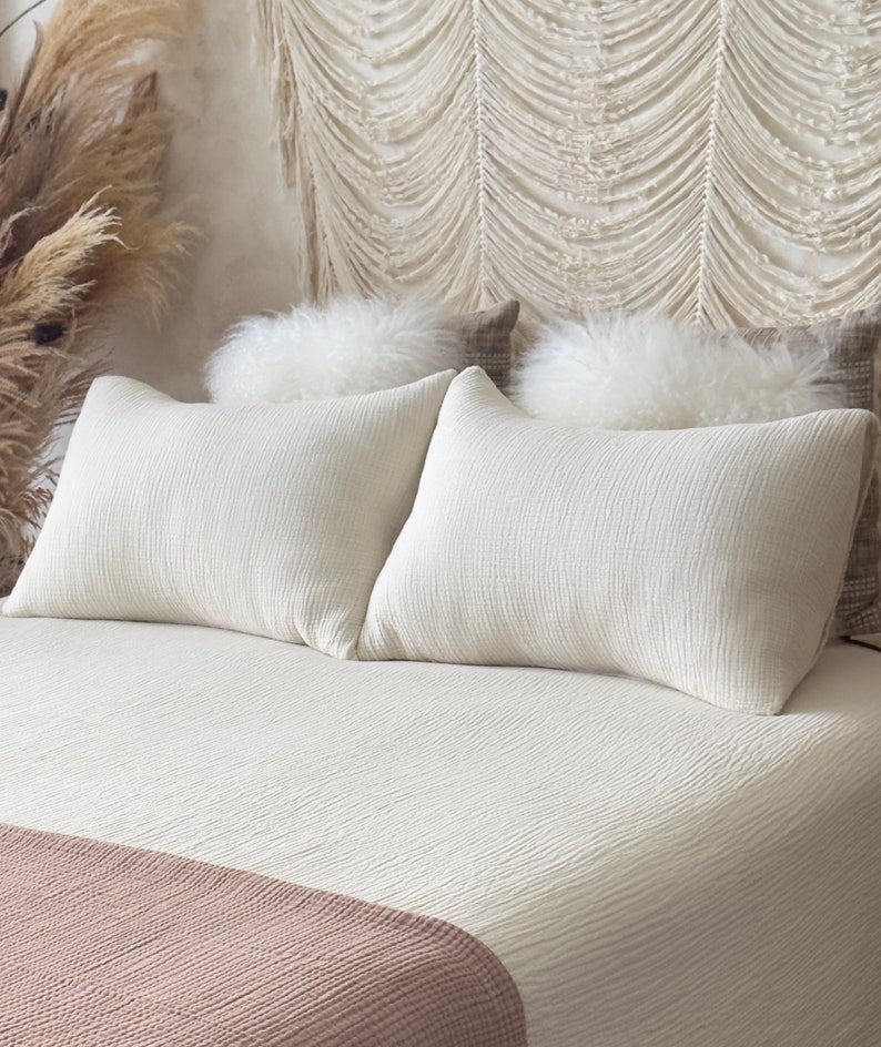 May include: A white bed with a white quilt and two white pillows. The bed has a pink throw blanket at the foot of the bed.