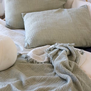 May include: A sage green waffle-textured throw blanket with a fringe edge is draped over a bed with matching sage green pillowcases.
