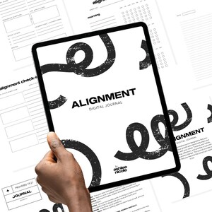 May include: A black tablet showing the text "ALIGNMENT DIGITAL JOURNAL" in a bold font, with a large, abstract black swirl design. Other pages with journal prompts are visible. The tablet is held in a hand.