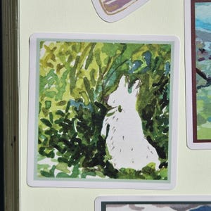 May include: A watercolor painting of a white rabbit sitting in a green bush. The rabbit is facing away from the viewer and looking up. The bush is made up of many small green leaves.