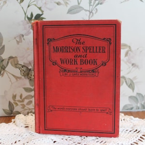 May include: A red hardcover book titled The Morrison Speller and Work Book by J. Cayce Morrison. The front cover features black text and a decorative border, with the subtitle The words everyone should learn to spell printed at the bottom.