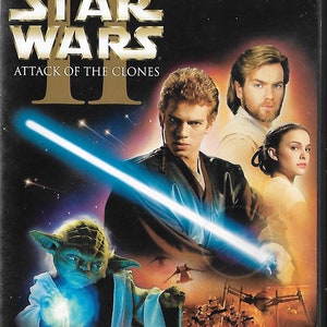 May include: DVD case for "Star Wars: Attack of the Clones." The cover features Anakin Skywalker holding a blue lightsaber, with Yoda, Obi-Wan Kenobi, and Padmé Amidala. The background is a space scene with the text "Star Wars II" in gold.