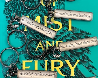 May include: Keychains with quotes from a book, featuring silver-toned metal chains and key rings. Each rectangular charm has a quote in black text on a white background. The keychains are displayed on a book cover with teal and yellow text.