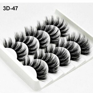 May include: Five pairs of black false eyelashes in a white plastic case. The eyelashes are arranged in rows, with the longest lashes at the top and the shortest lashes at the bottom. The case has the text "3D-47" printed on it.