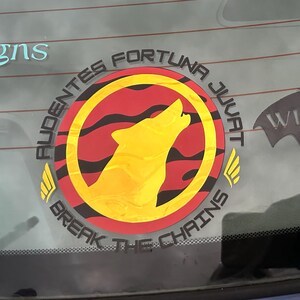 Puede incluir: Adhesivo circular con un lobo aullando amarillo dentro de un c&iacute;rculo rojo con rayas negras. El adhesivo tiene el texto "AUDENTES FORTUNA JUVAT" y "BREAK THE CHAINS".