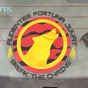 Puede incluir: Una pegatina circular con un lobo amarillo aullando dentro de un c&iacute;rculo rojo con rayas negras. La pegatina tiene el texto "AUDENTES FORTUNA JUVAT" y "BREAK THE CHAINS" en negro, con detalles de alas amarillas.