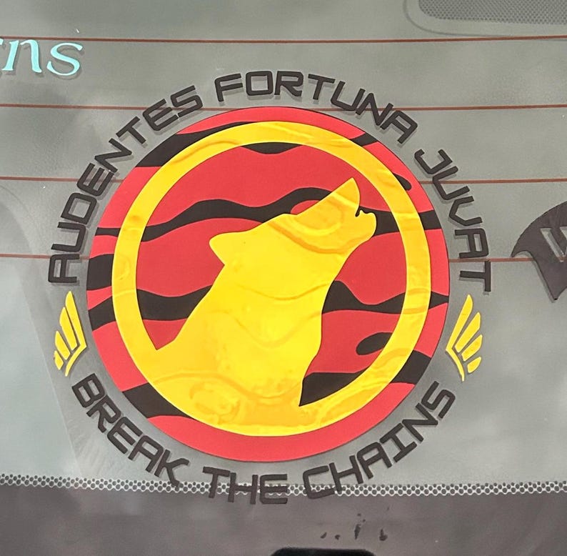 Puede incluir: Una pegatina circular con un lobo amarillo aullando dentro de un c&iacute;rculo rojo con rayas negras. La pegatina tiene el texto "AUDENTES FORTUNA JUVAT" y "BREAK THE CHAINS" en negro, con detalles de alas amarillas.