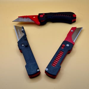May include: Three utility knives with black and red handles and silver blades are displayed against a yellow background. The knives have a textured grip and a blade that can be retracted. The top knife is fully extended, while the other two are partially open.