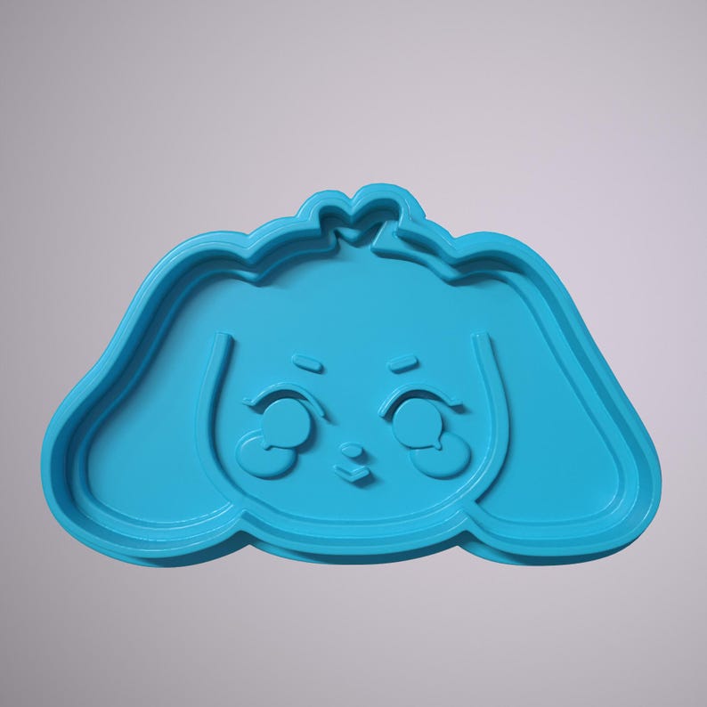 May include: A blue plastic cookie cutter shaped like a cartoon dog with big eyes and a small nose.