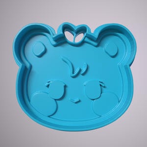 May include: A blue plastic cookie cutter shaped like a cartoon animal with a bow on its head. The animal has large eyes and a small mouth.