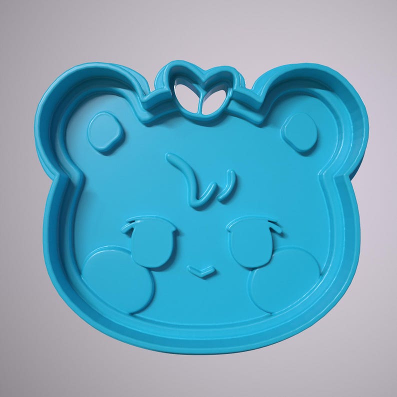 May include: A blue plastic cookie cutter shaped like a cartoon animal with a bow on its head. The animal has large eyes and a small mouth.