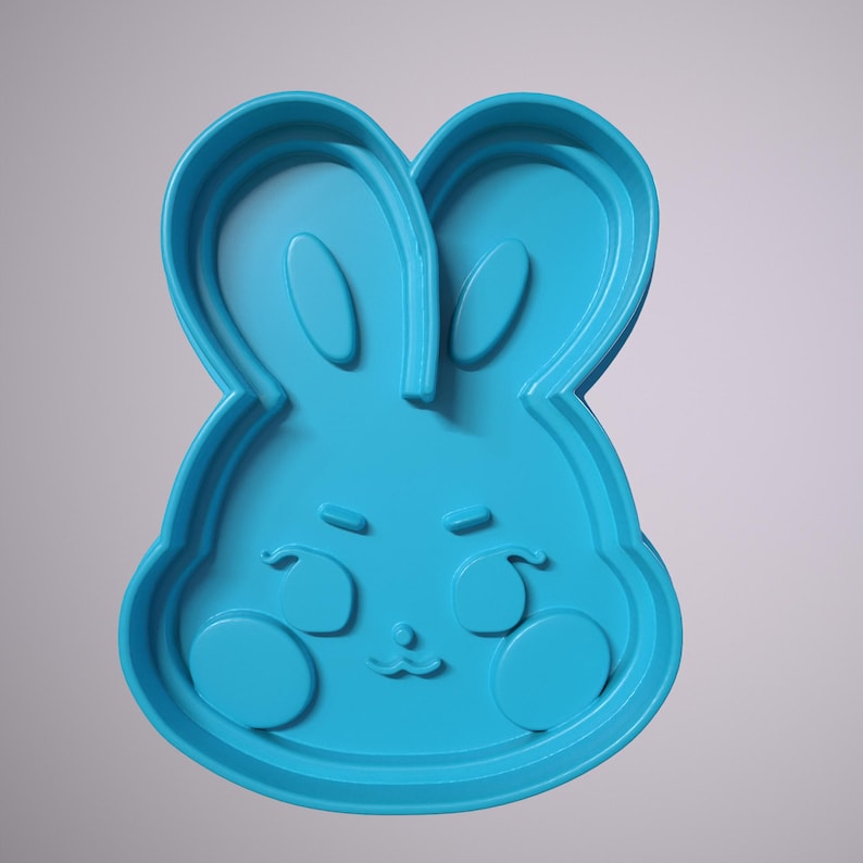 May include: A blue plastic cookie cutter shaped like a bunny rabbit with a cute face. The bunny has big ears, a small nose, and two large circles for cheeks.