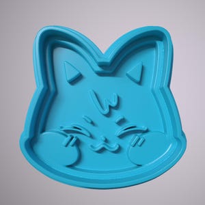 May include: A blue plastic cookie cutter shaped like a cat with a cute expression. The cat has a small nose, big eyes, and a small mouth. The cat is blushing and has its paws on its cheeks.