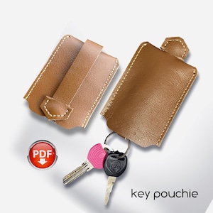 May include: Two brown leather key pouches with a key ring and keys. The pouches have a flap with a stitched edge. The text "key pouchie" is printed below the pouches.