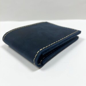 May include: A dark blue leather wallet with white stitching. The wallet is folded in half and the stitching is visible on the edges.