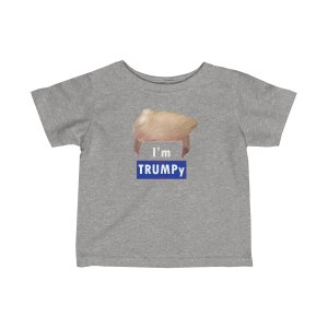 Könnte beinhalten: Ein graues T-Shirt für Kleinkinder mit einer blonden Perücke und dem Text "I'm TRUMPY" in Blau.