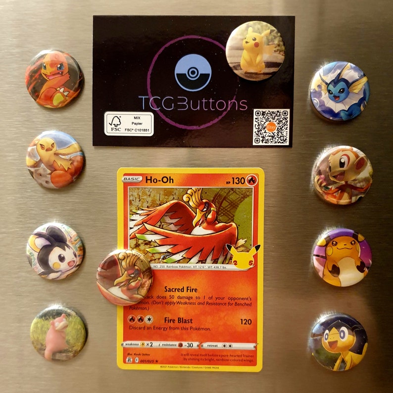 May include: A collection of round, colorful buttons featuring various Pok&eacute;mon characters, alongside a Pok&eacute;mon trading card. The card displays a Ho-Oh illustration. The buttons and card are arranged on a metallic surface.