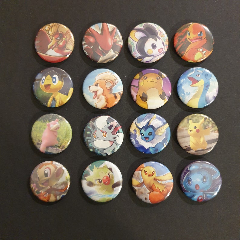 May include: A collection of sixteen round pinback buttons featuring various colorful Pok&eacute;mon characters. Each button displays a different character illustration, with a variety of designs and backgrounds. The buttons are arranged in four rows of four on a dark surface.