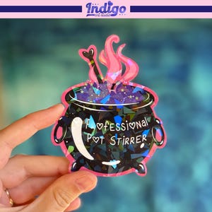 May include: A sticker featuring a black cauldron with a pink outline and accents. The cauldron has a holographic effect and pink smoke rising from it. The text "A Professional Pot Stirrer" is written on the cauldron.