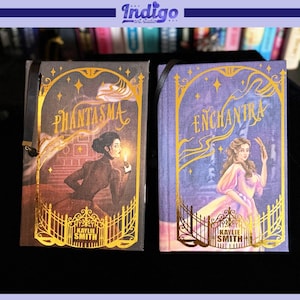 May include: Two fantasy-themed books with gold foil accents. The book on the left is titled "Phantasma" and features a woman holding a candle. The book on the right is titled "Enchantra" and features a woman in a pink dress. Both books have a black ribbon bookmark.