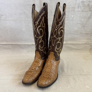 Könnte beinhalten: Ein Paar hohe Cowboystiefel mit einem dunkelbraunen Lederschaft, verziert mit aufwendigen goldfarbenen Stickereien und kleinen weißen Akzenten. Der untere Fußbereich besteht aus strukturiertem, hellbraunem Schlangenledermaterial.