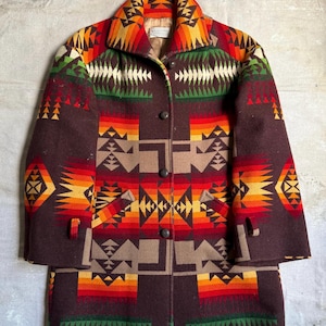 Könnte beinhalten: Ein brauner Wollmantel mit einem farbenfrohen geometrischen Muster in Rot-, Orange-, Gelb-, Grün- und Weißtönen. Der Mantel hat einen Kragen, einen Knopfverschluss und zwei Taschen. Der Mantel ist lang.