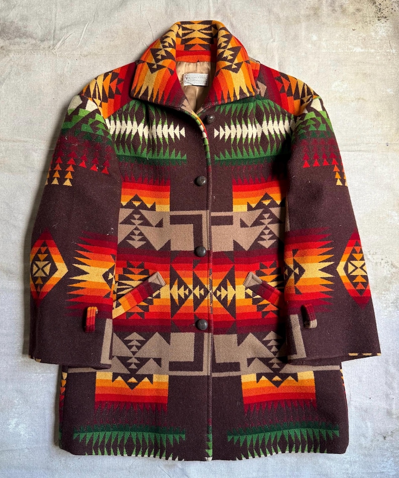 Puede incluir: Un abrigo de lana marr&oacute;n con un colorido estampado geom&eacute;trico en tonos rojos, naranjas, amarillos, verdes y blancos. El abrigo tiene cuello, cierre de botones y dos bolsillos. El abrigo es largo.