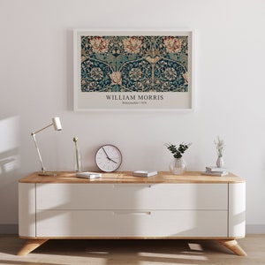 May include: A white framed print of a vintage William Morris Honeysuckle design in a teal and gold color scheme. The print is hanging on a white wall above a white dresser with two drawers. The dresser has a light wood top and legs.