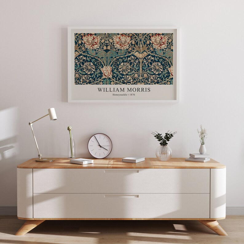 May include: A white framed print of a vintage William Morris Honeysuckle design in a teal and gold color scheme. The print is hanging on a white wall above a white dresser with two drawers. The dresser has a light wood top and legs.