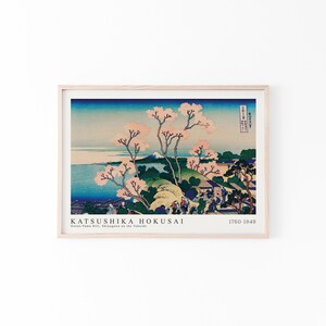 May include: A woodblock print by Katsushika Hokusai titled "Goten-Yama Hill, Shinagawa on the Tokaido" depicting a landscape with a mountain in the distance, cherry blossoms, and people walking on a path. The print is framed in a light wood frame.