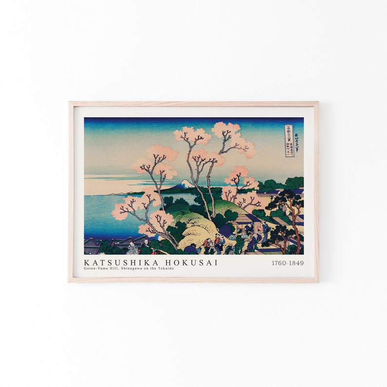 May include: A woodblock print by Katsushika Hokusai titled "Goten-Yama Hill, Shinagawa on the Tokaido" depicting a landscape with a mountain in the distance, cherry blossoms, and people walking on a path. The print is framed in a light wood frame.