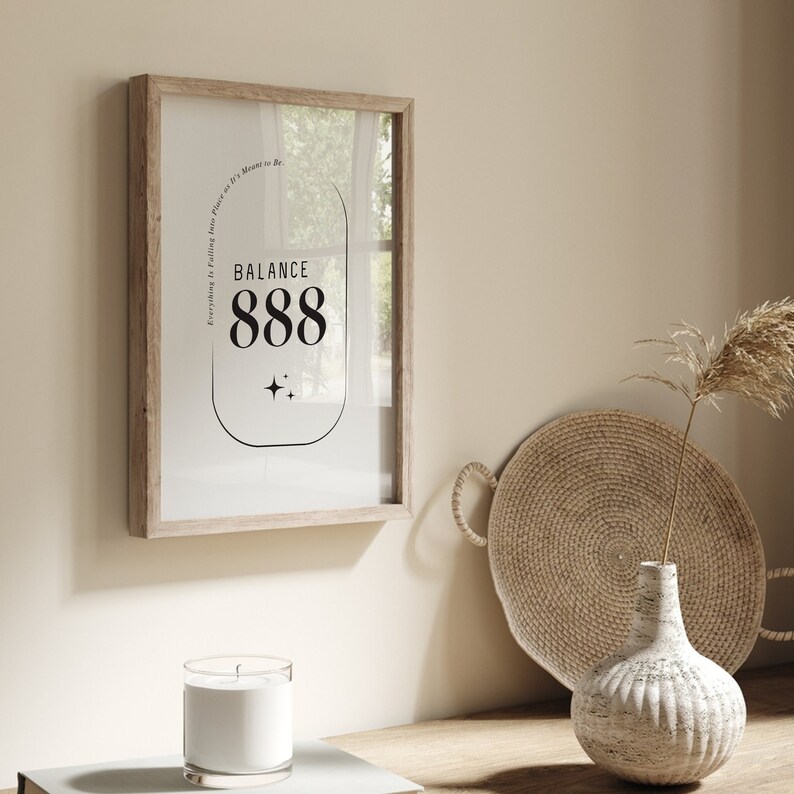 May include: A framed print with a white background and black text that reads "Balance 888 Everything is Falling into Place as It's Meant to Be". The print is in a light wood frame and is hanging on a beige wall.