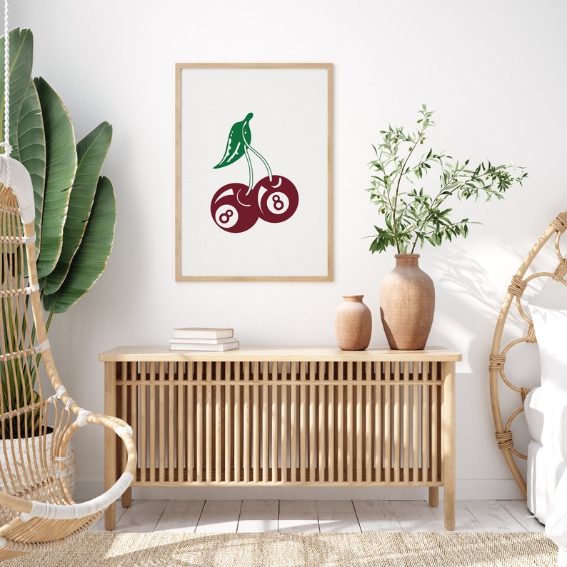 May include: A framed print of a red cherry with a green stem and leaves. The cherry is made up of two 8-ball pool balls.