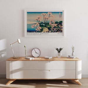 May include: A framed print of a Japanese woodblock print by Katsushika Hokusai, titled "Great Wave off Kanagawa". The print depicts a large wave crashing over a boat with Mount Fuji in the background. The print is framed in a white frame and is hanging on a white wall.