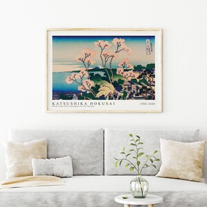 May include: A vintage wood-framed print of a Japanese landscape painting by Katsushika Hokusai. The painting depicts a mountain range with a river and cherry blossoms in the foreground. The text "KATSUSHIKA HOKUSAI" and "1760-1849" is printed below the image.