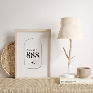 May include: A framed print with a black and white design featuring the text "BALANCE 888" and the phrase "Everything is falling into place as it's meant to be." The print is on a wooden table with a lamp and a book titled "Philosophy".