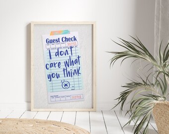Puede incluir: Una impresión enmarcada de un cheque de restaurante azul y blanco con el texto "I don't care what you think" en azul. El cheque tiene una caricatura de una cara dormida con una lágrima que sale de su ojo. El marco es de madera clara y el fondo es blanco.