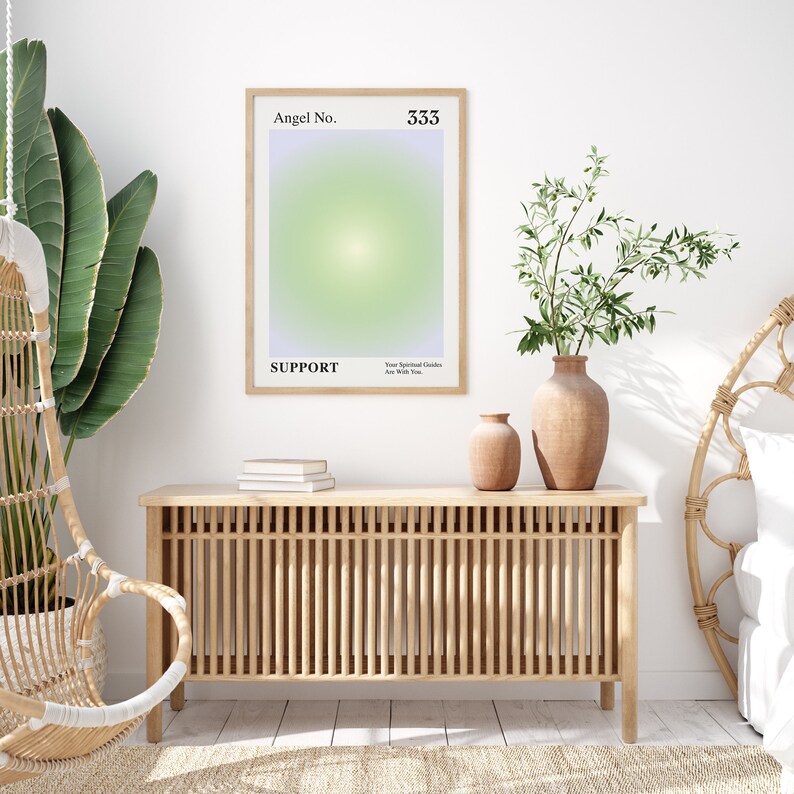 May include: A framed poster with a light green and purple gradient background. The poster has the text "Angel No. 333" and "SUPPORT" in black text. The text "Your Spiritual Guides Are With You" is also in black text. The poster is hanging on a white wall above a wooden cabinet with a slatted front.