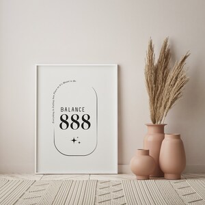 May include: White framed print with black text that reads "Everything is Falling into Place as it's Meant to Be. BALANCE 888" with two small stars below the number. The print is on a white wall with a beige rug in front of it. Three beige vases with dried pampas grass in the tallest vase.