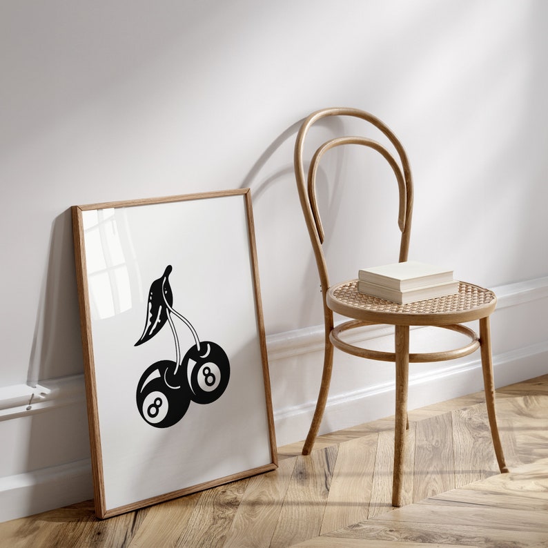 May include: A black and white illustration of two cherries with the number "8" on each. The illustration is framed in a light wood frame and is hanging on a white wall.